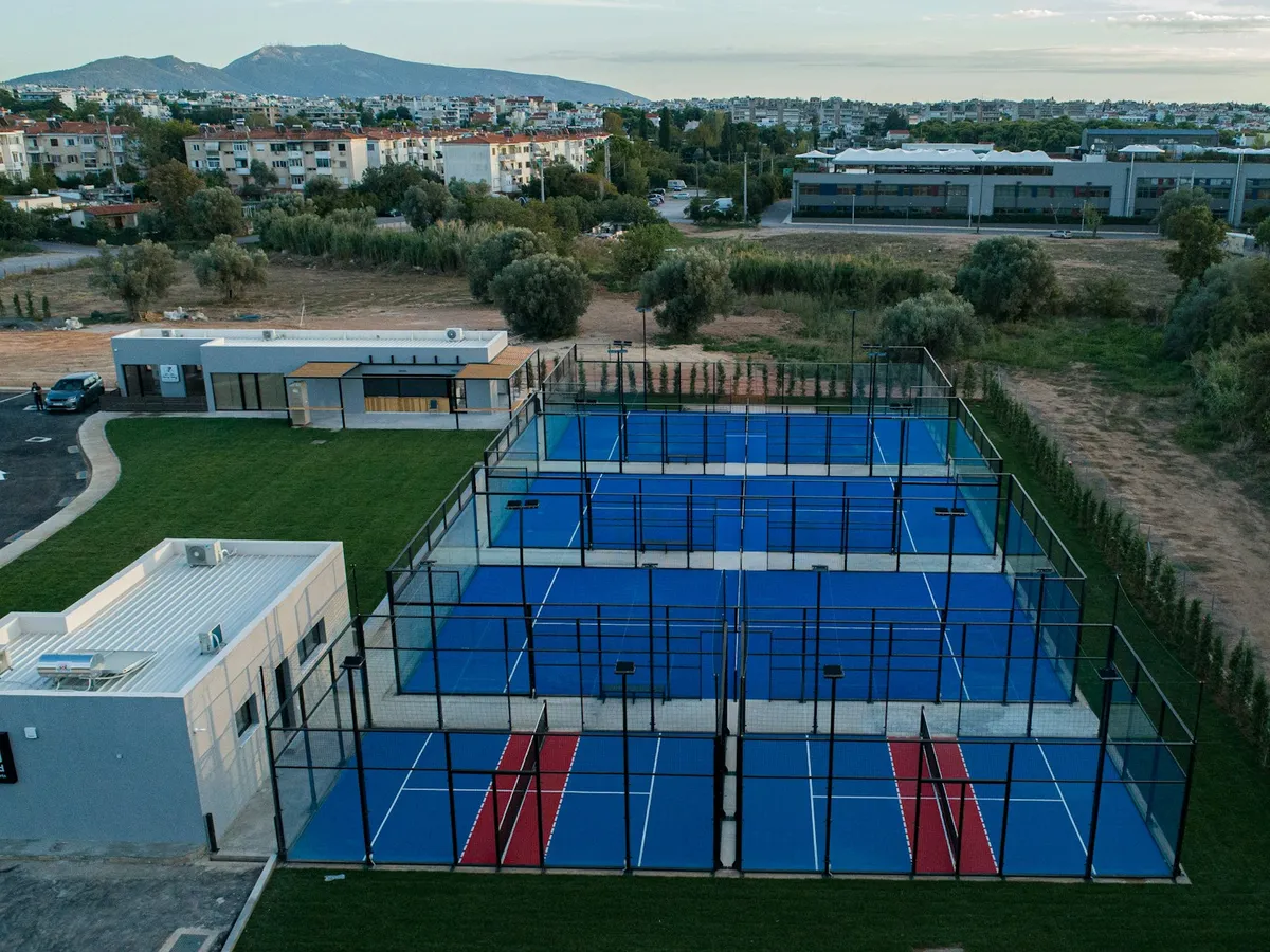 Aerial view of padel courts near homes, with a clubhouse and a car park next to the glass courts